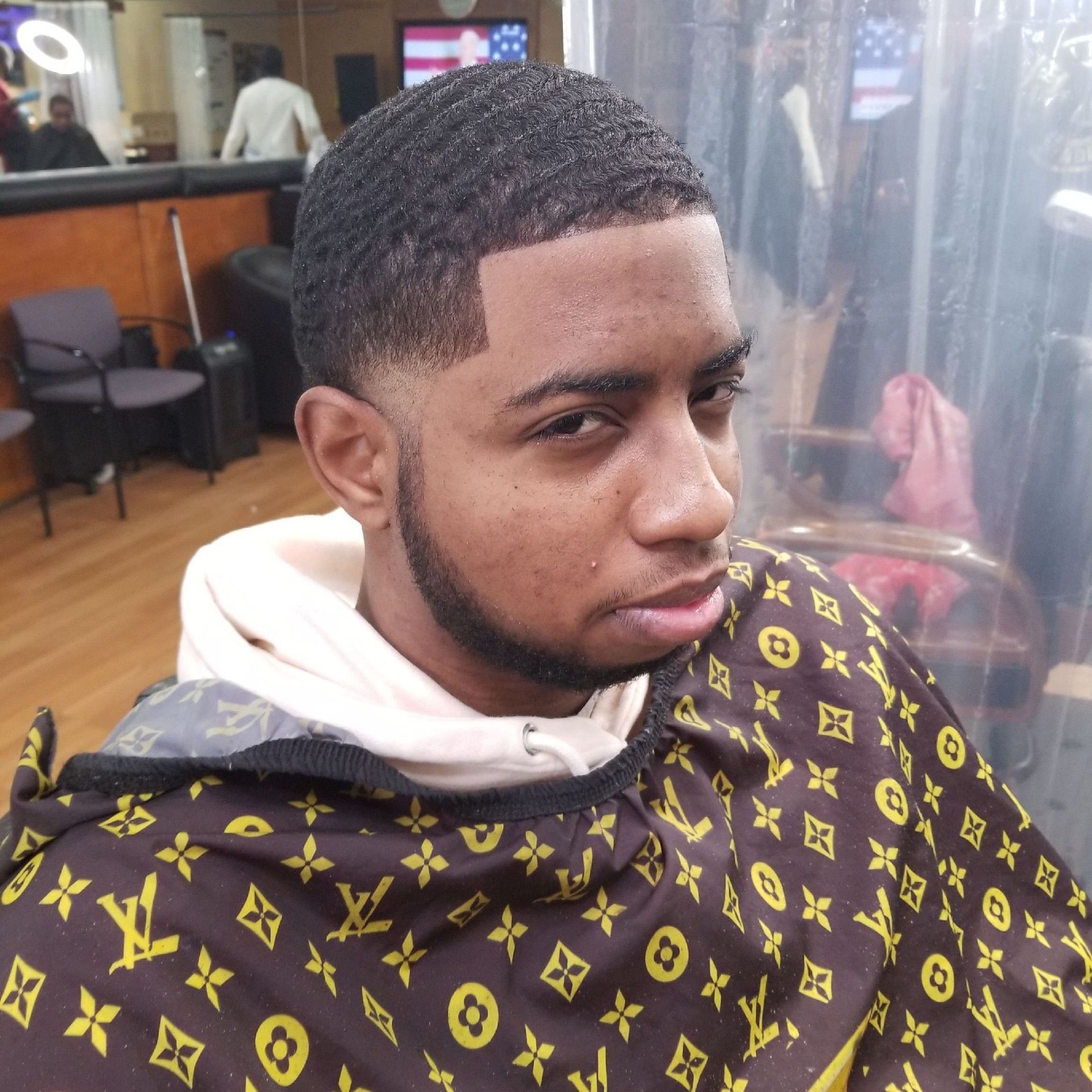 Man in barber cape with a textured haircut and trimmed beard, looking at camera.