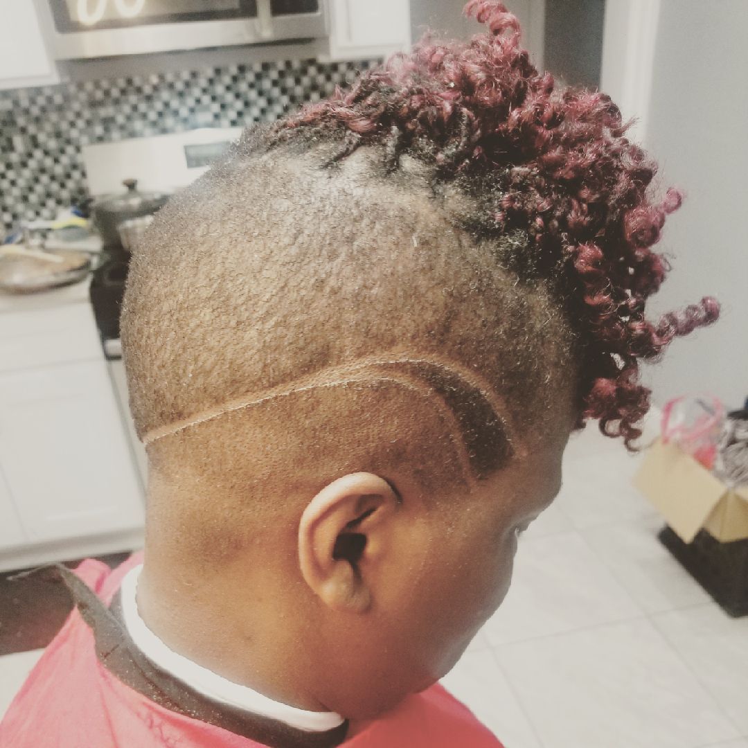 Person with short hair, shaved sides, and red curls on top. A curved design is shaved on the side of the head.