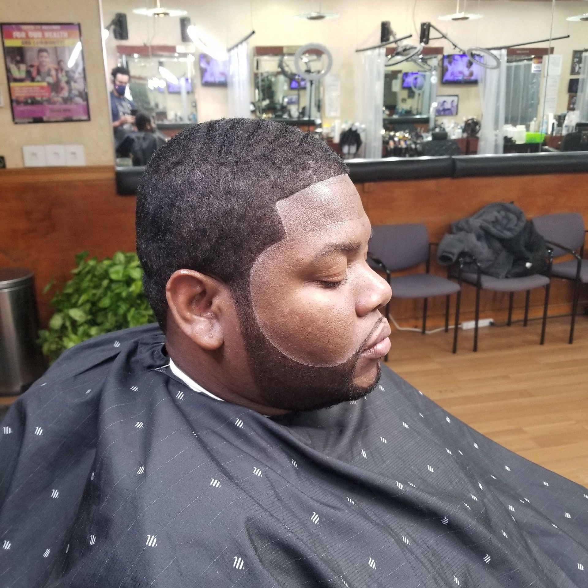 Man in barber chair, hair cut and beard trim, salon setting, wearing cape.