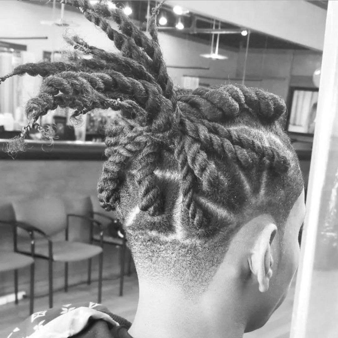 Twisted hairstyle with shaved design on the back of the head. Indoors, with chairs in the background.