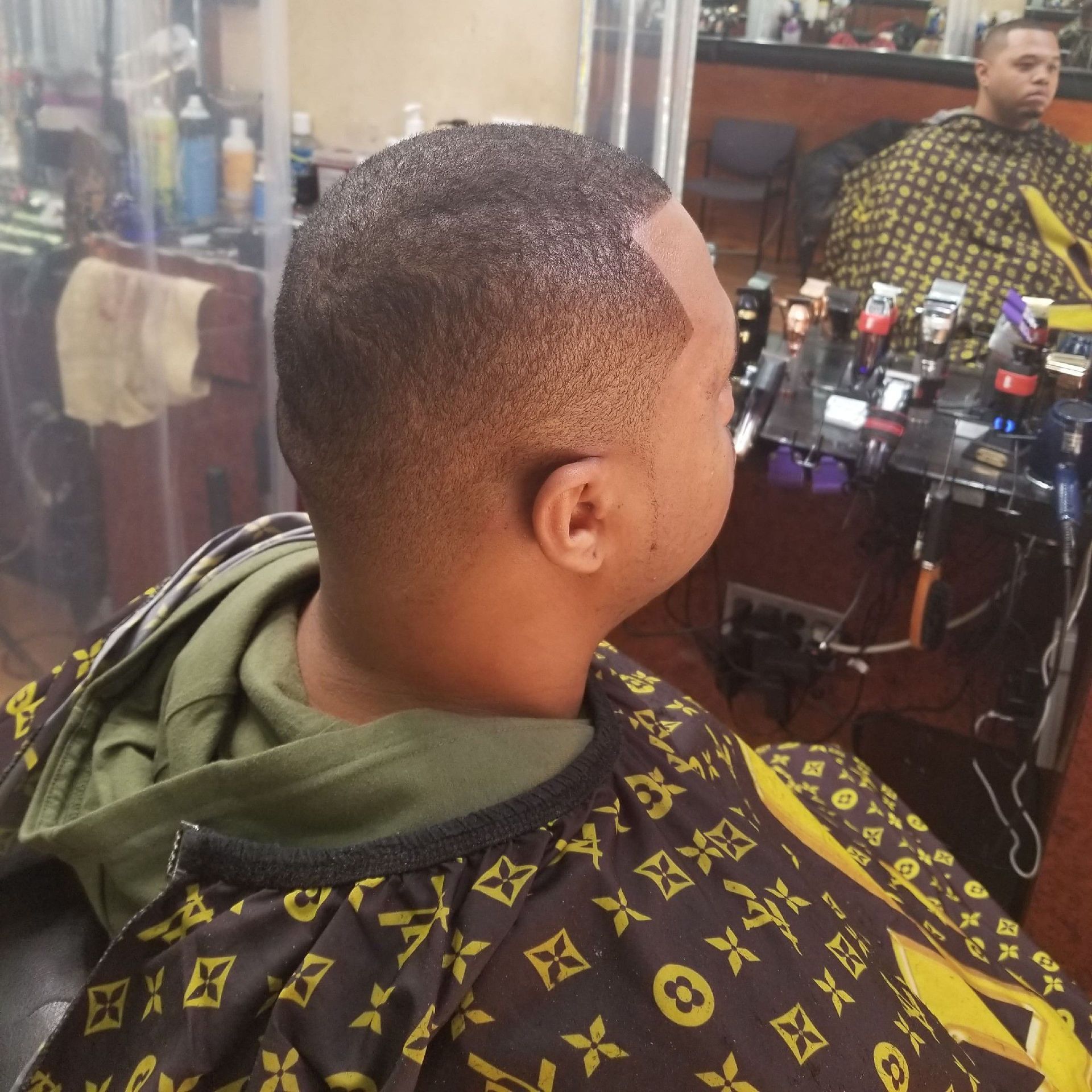 Person getting a haircut in a barbershop; low fade hairstyle.