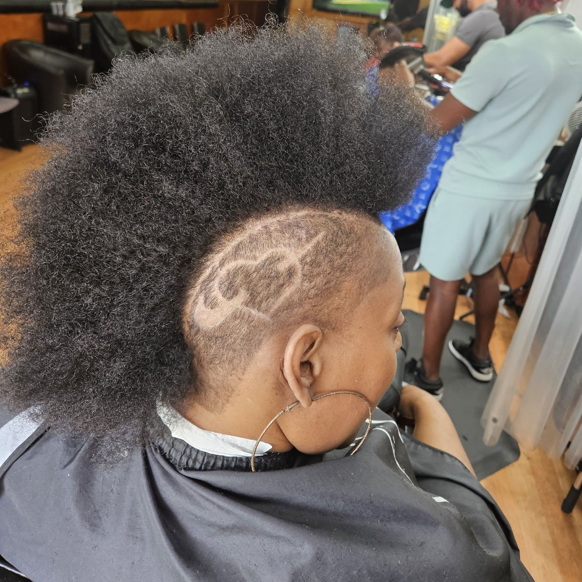 Person with a dark afro and shaved sides, hair design on the side of their head, in a barbershop.