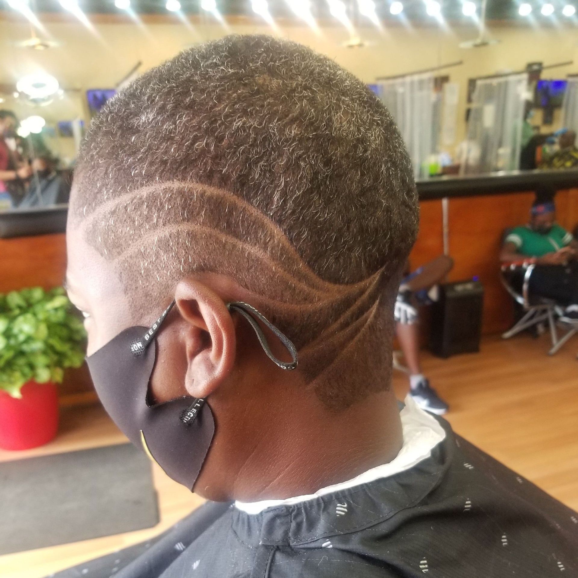 Person with short, patterned haircut wearing a face mask in a barbershop.