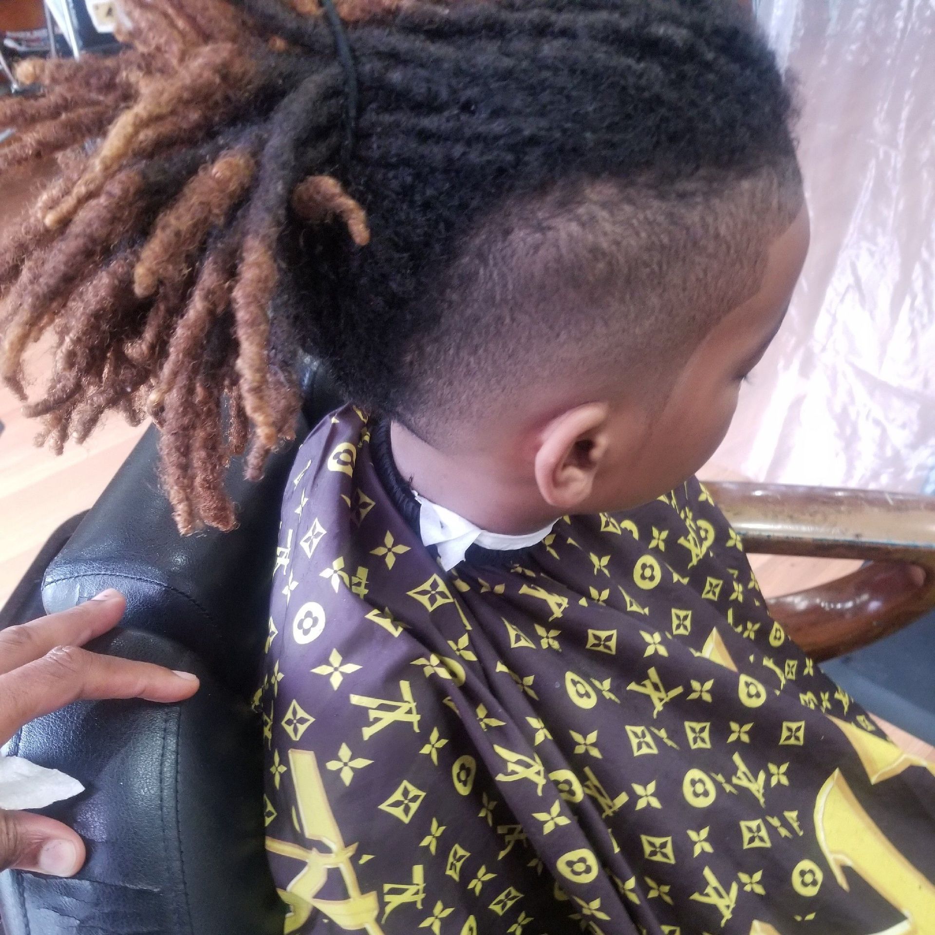 Child with a fade haircut and dreadlocks, wearing a barber cape.