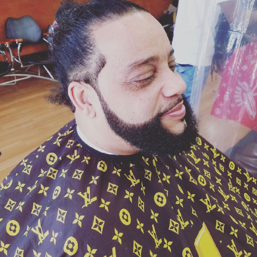Man with a beard getting a haircut, wearing a patterned cape in a salon.