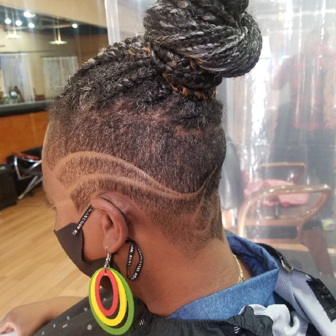 Woman with braided updo and shaved side, wearing a face mask and earrings, in a salon.