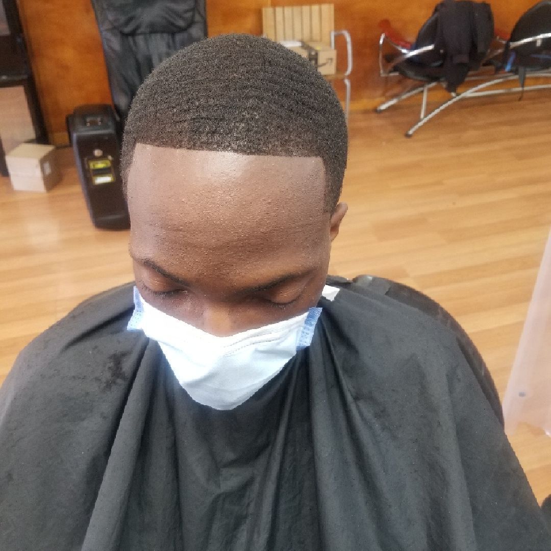 Person with short, wavy hair, wearing a face mask and black cape in a salon.