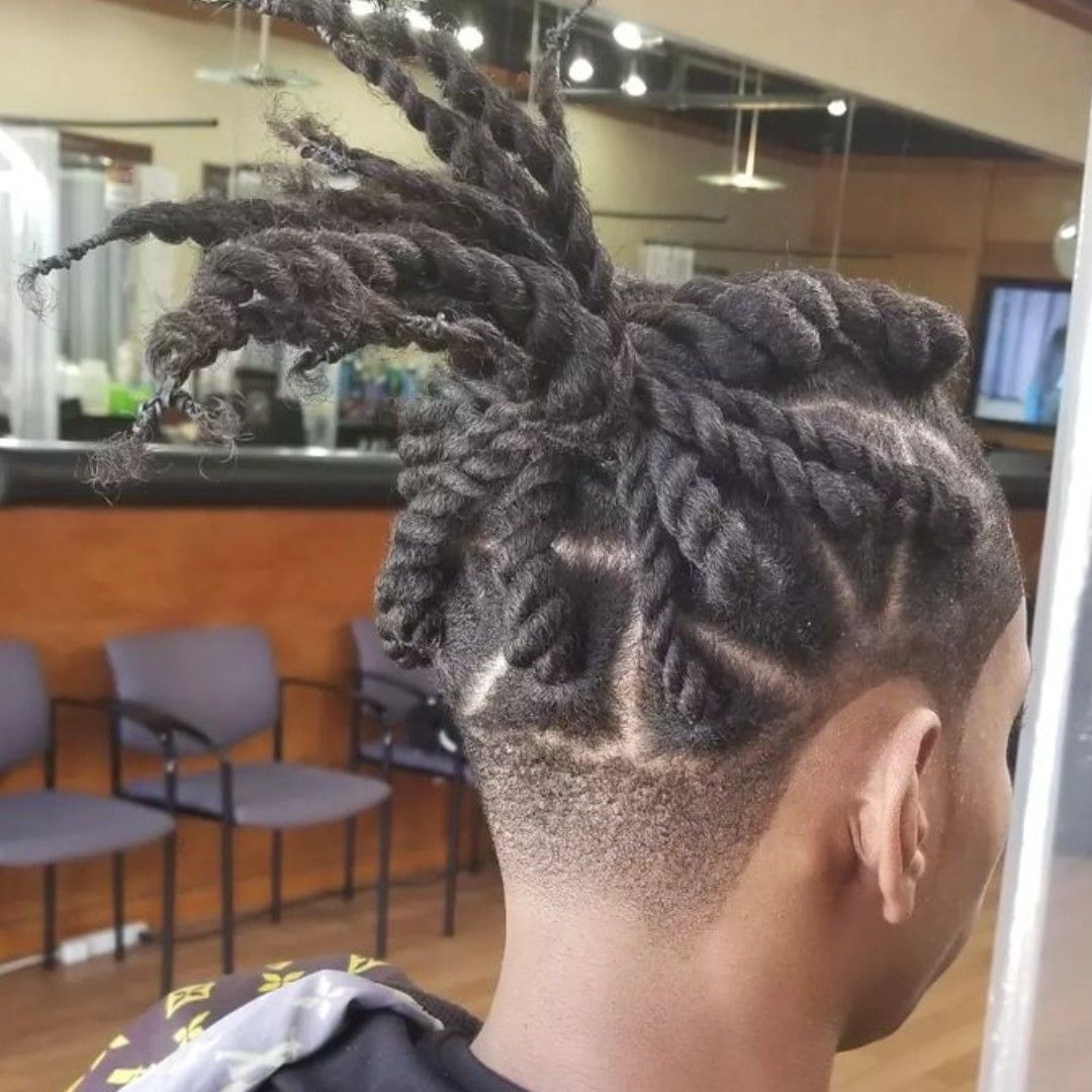 Man with thick twisted dreadlocks styled up, with a patterned shaved design on the side of his head.