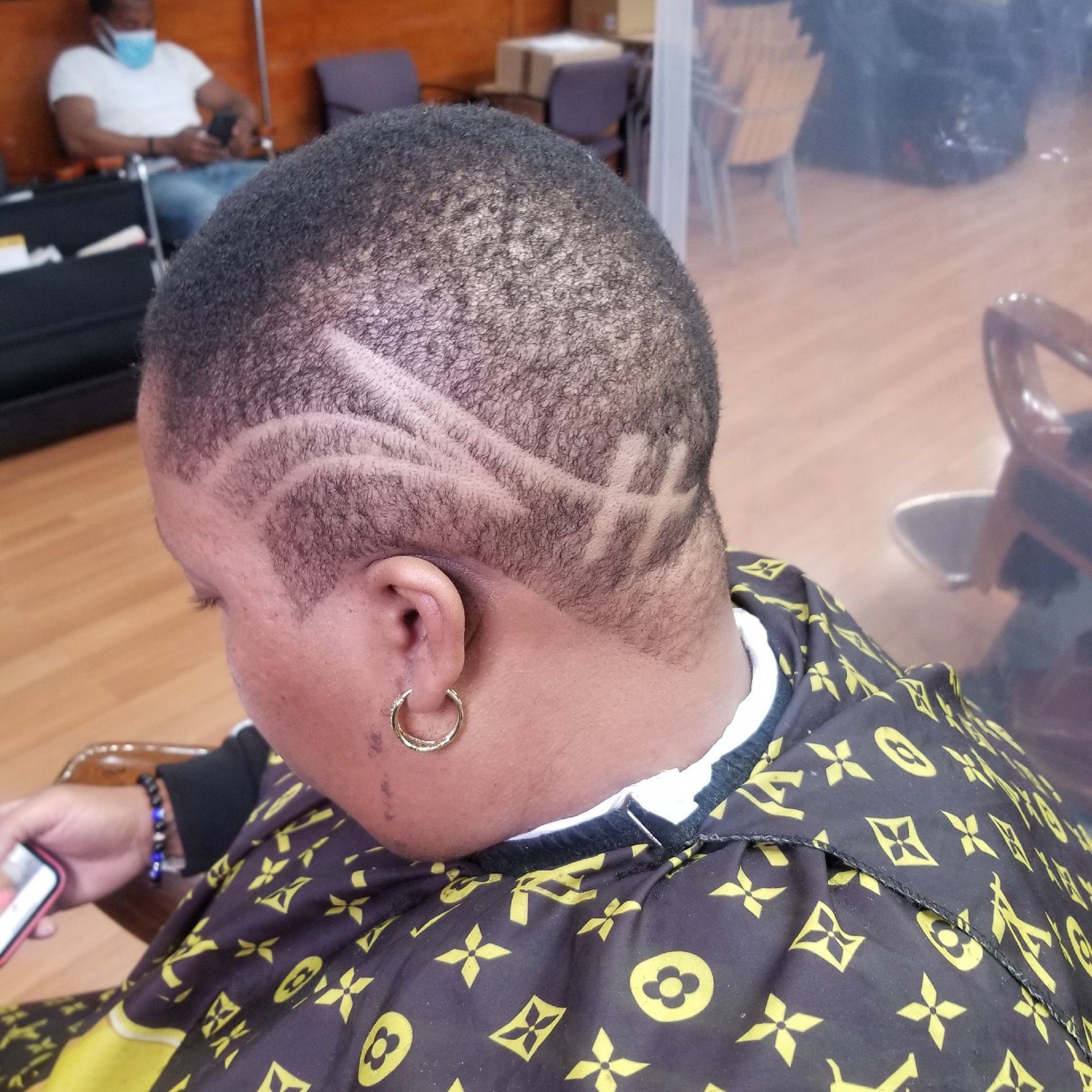 Person with a shaved head and hair design, wearing a patterned cape in a salon.