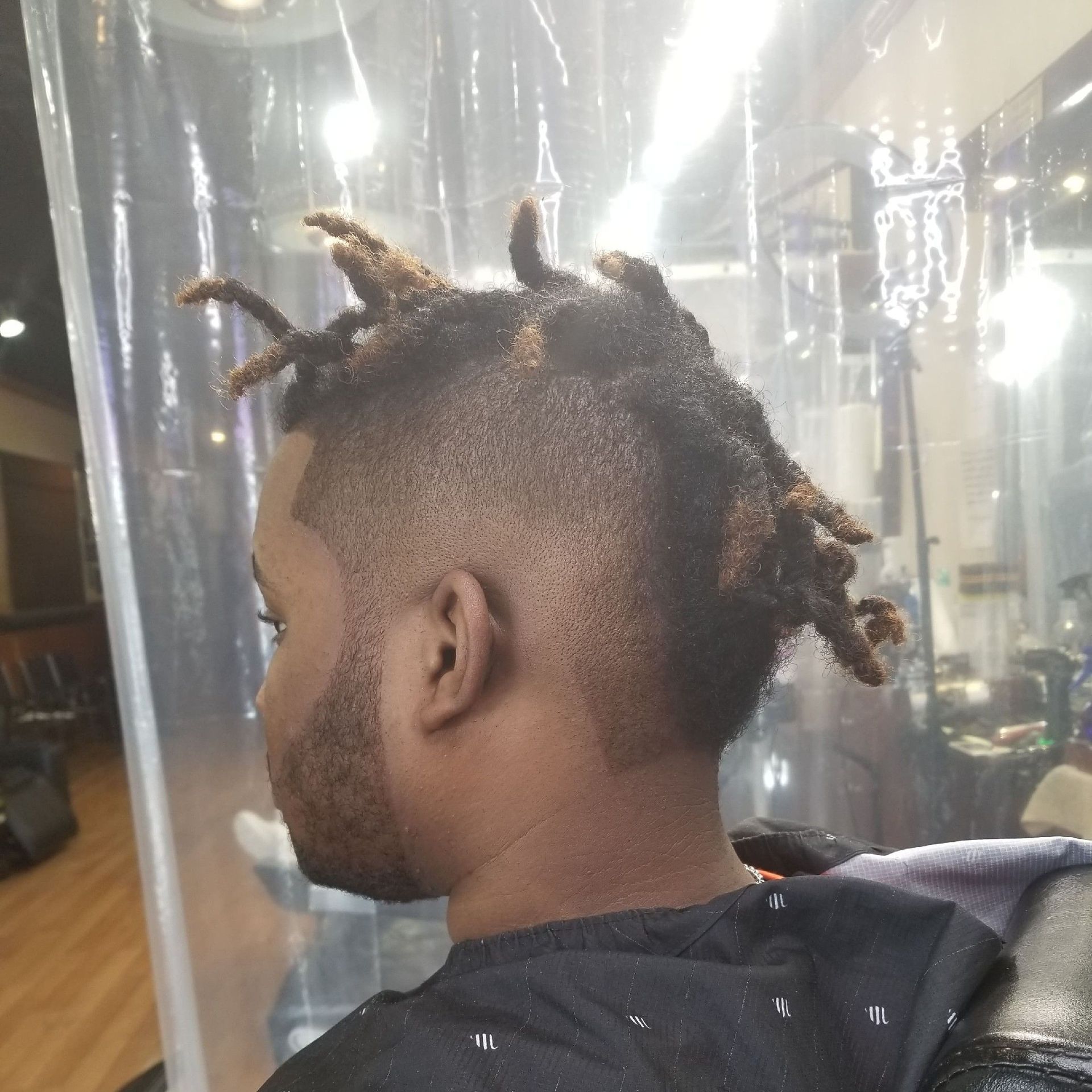 Man with a faded haircut, short dreads on top, seated at a barber shop.