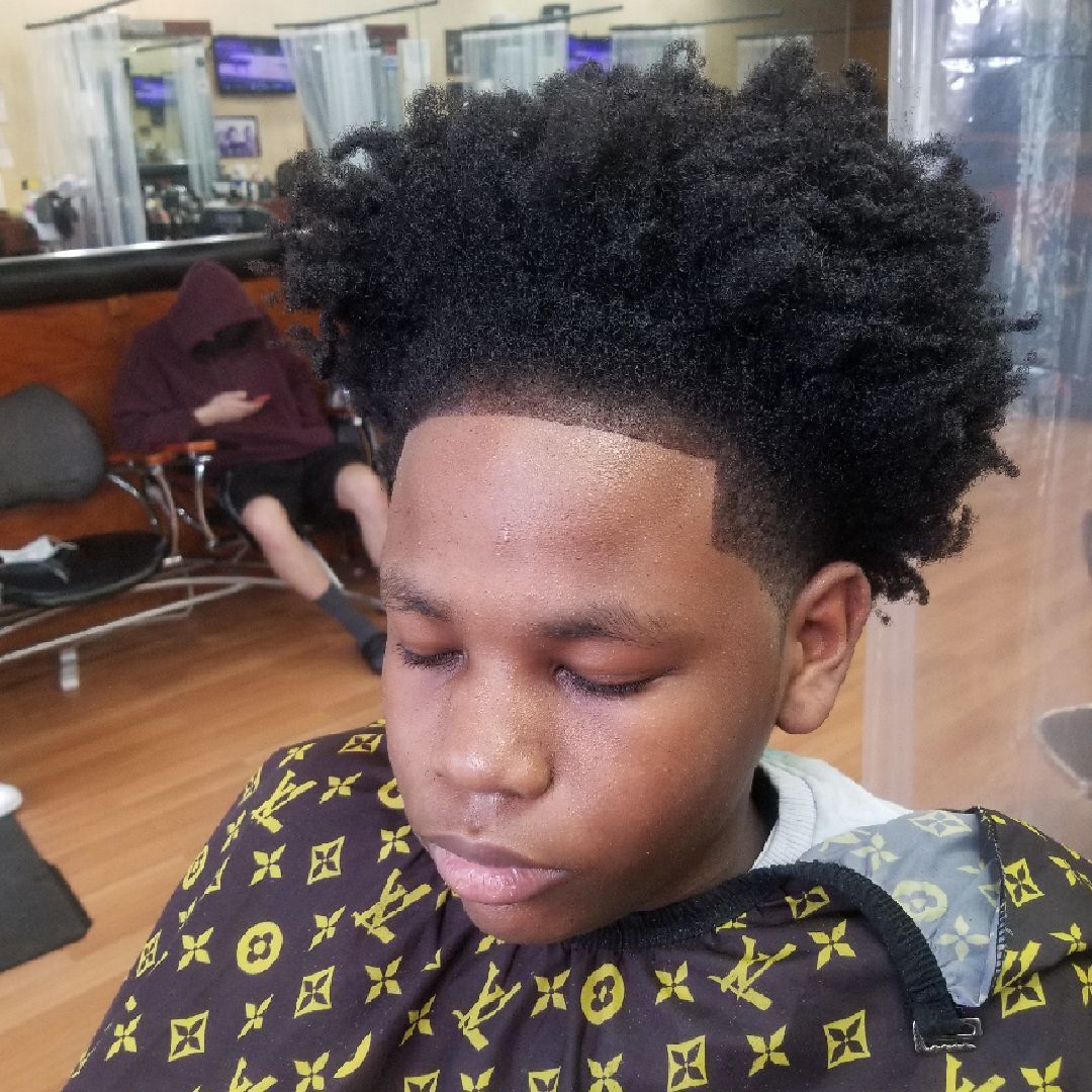 Young person with fresh haircut and a cape, inside a barber shop.
