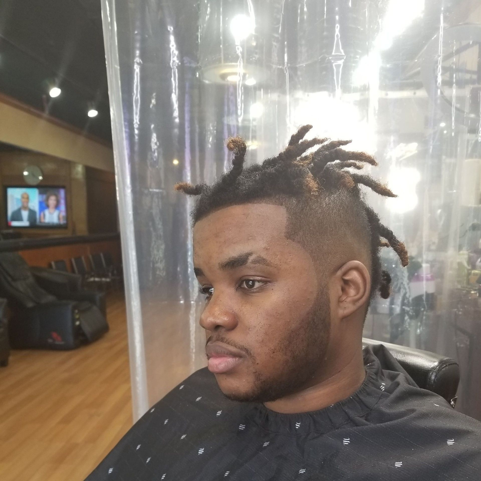 Man with dreadlocks and faded haircut at a salon, wearing a barber cape.