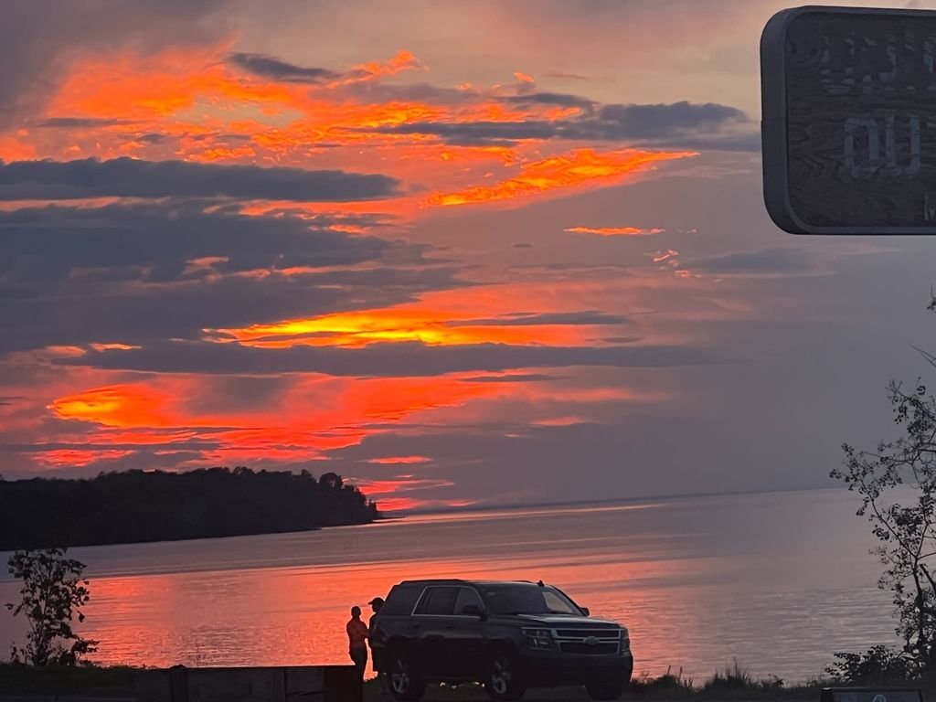 A car is parked in front of a sunset over a body of water.