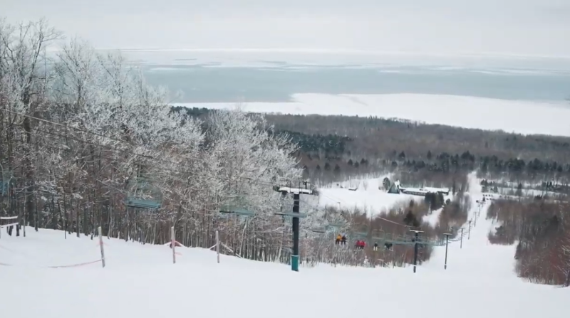 A ski lift is going down a snow covered slope.