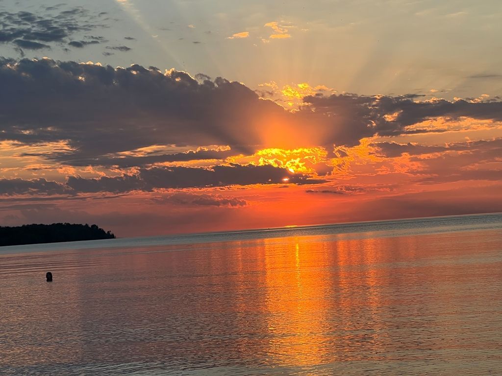 A sunset over a body of water with the sun shining through the clouds