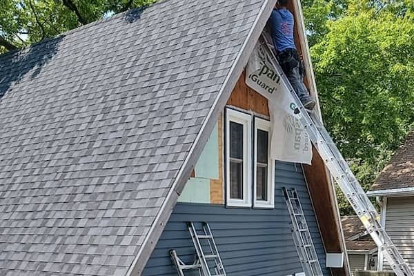 A man is working on the roof of a house with a ladder.