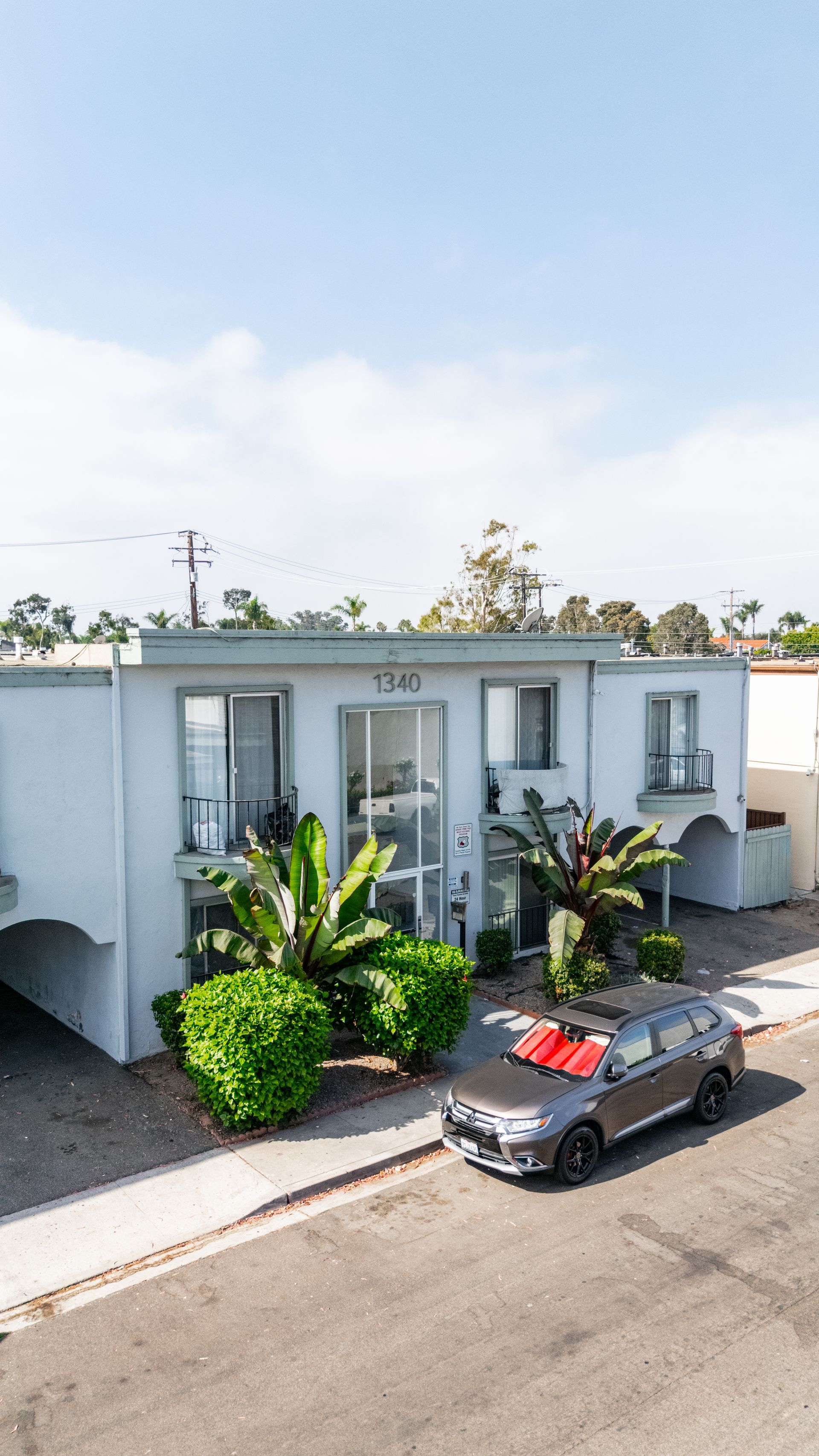 Gray car with red bows parked in front of a two-story white apartment building on a sunny day.