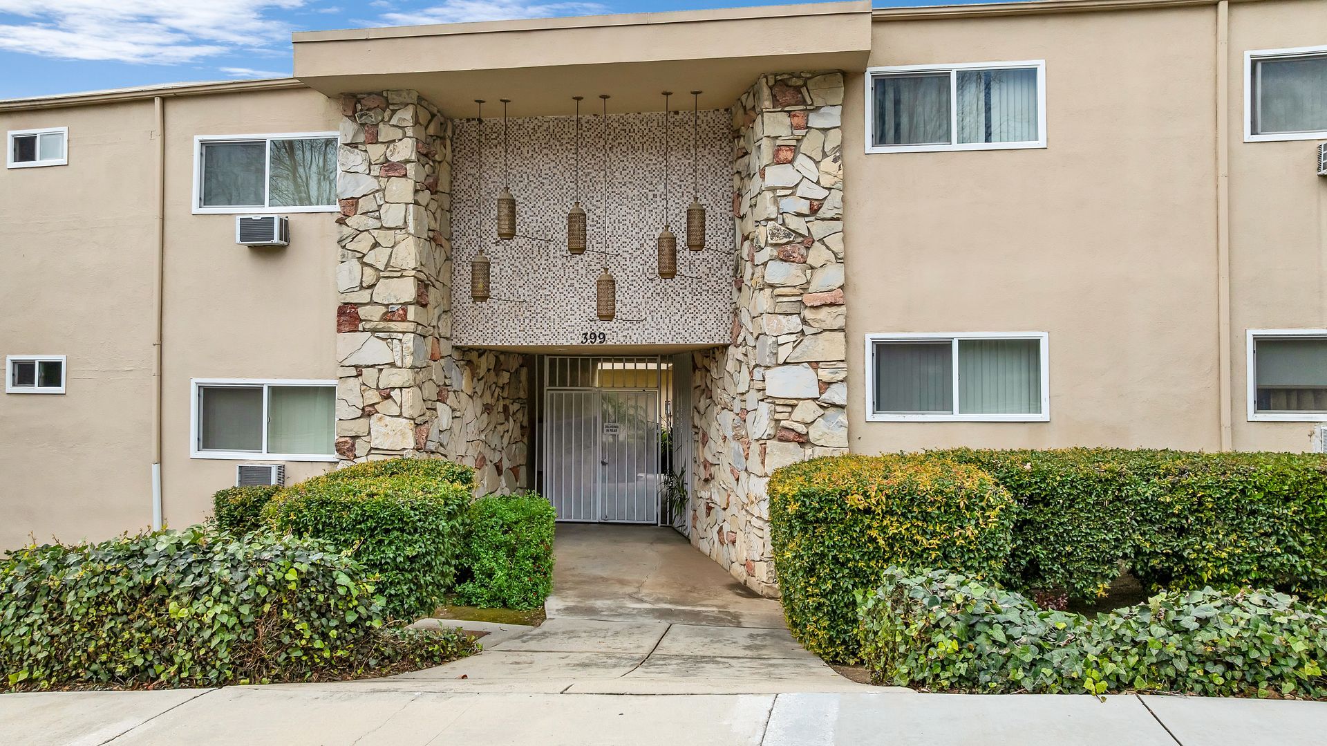 Apartment building exterior with beige walls, stone accents, and green bushes.