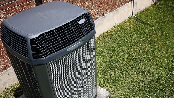 An air conditioner is sitting in the grass in front of a brick building.