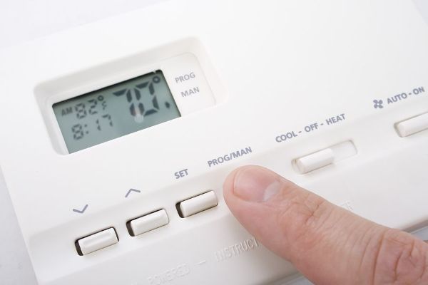 A person is pressing a button on a thermostat.