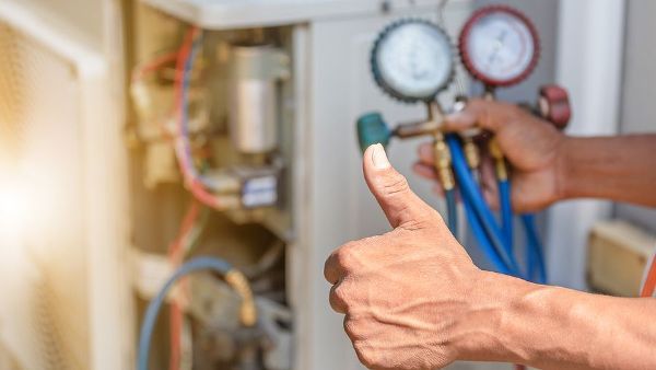 A man is giving a thumbs up while working on an air conditioner.