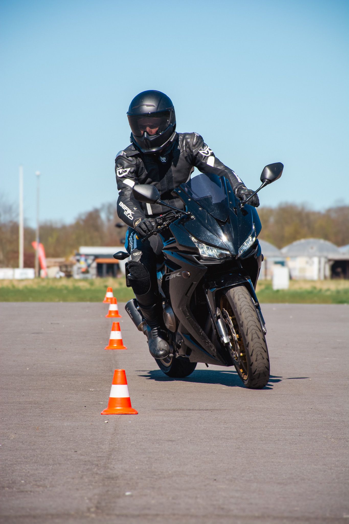 Een man rijdt op een motorfiets op een weg naast kegels.