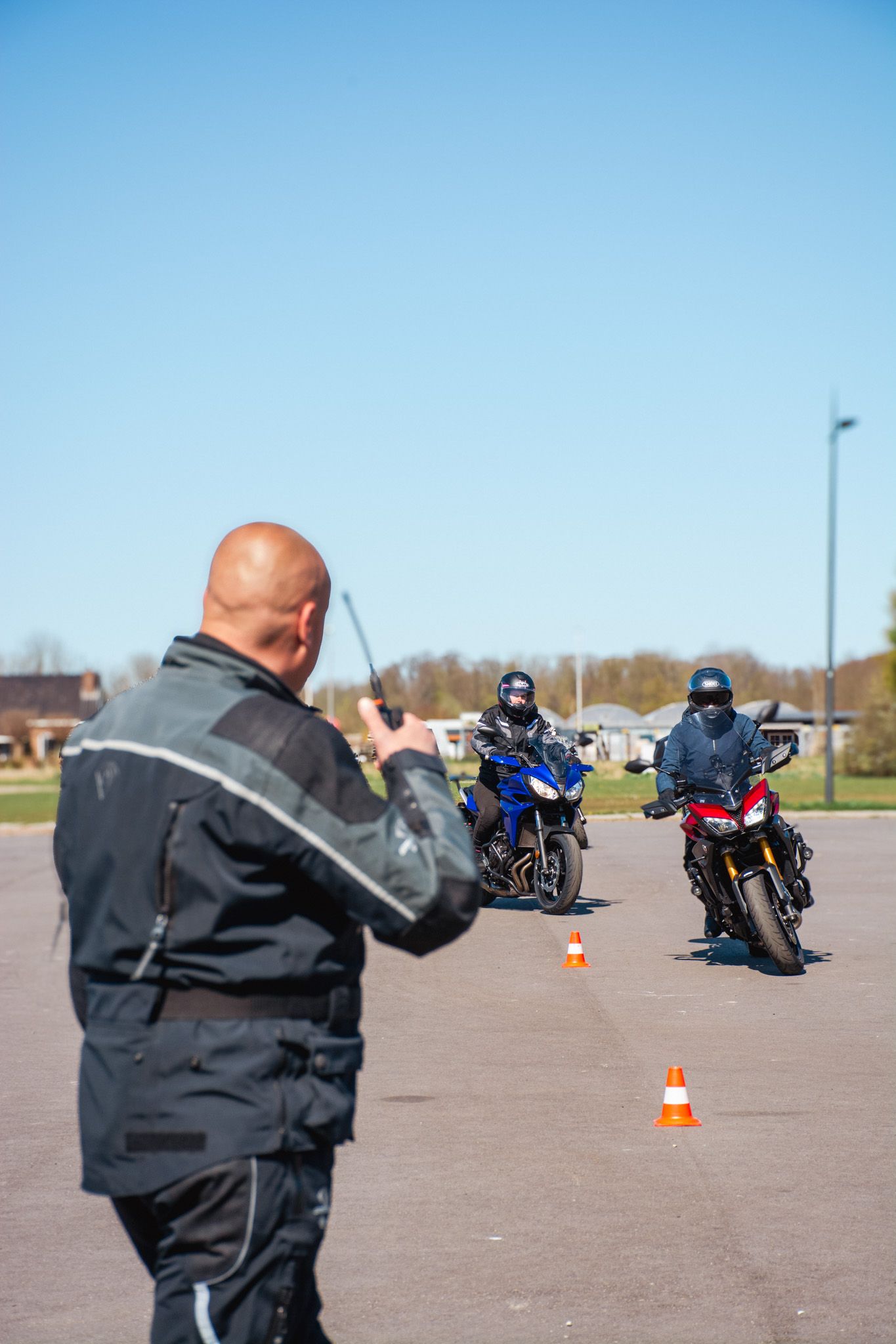 Een man praat via een portofoon, terwijl twee mannen op een motorfiets rijden.