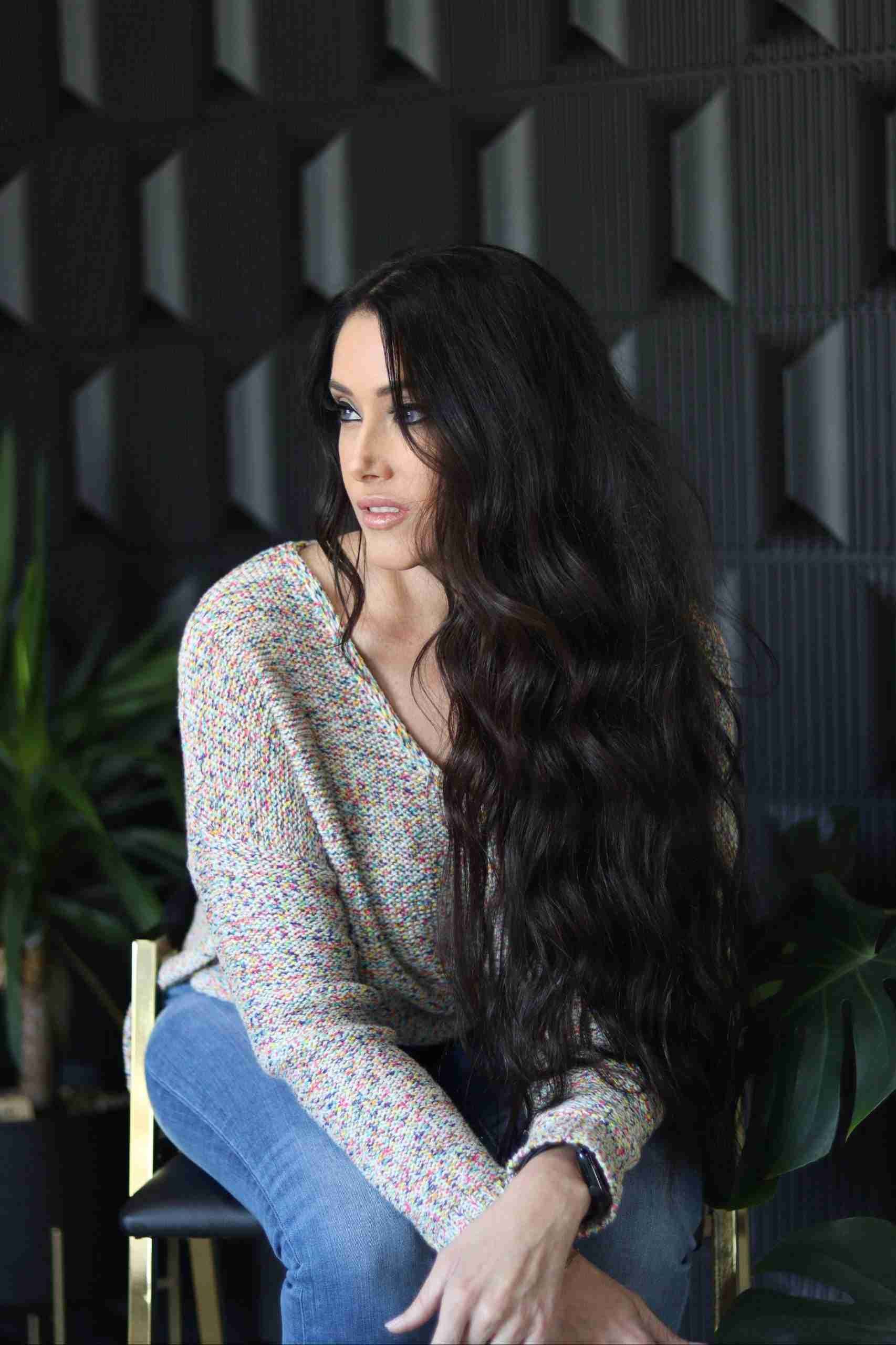A woman with long hair is sitting on a chair with her legs crossed.