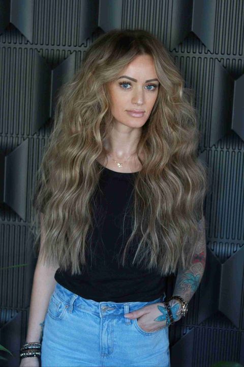 A woman with long blonde hair is wearing a black shirt and blue jeans.