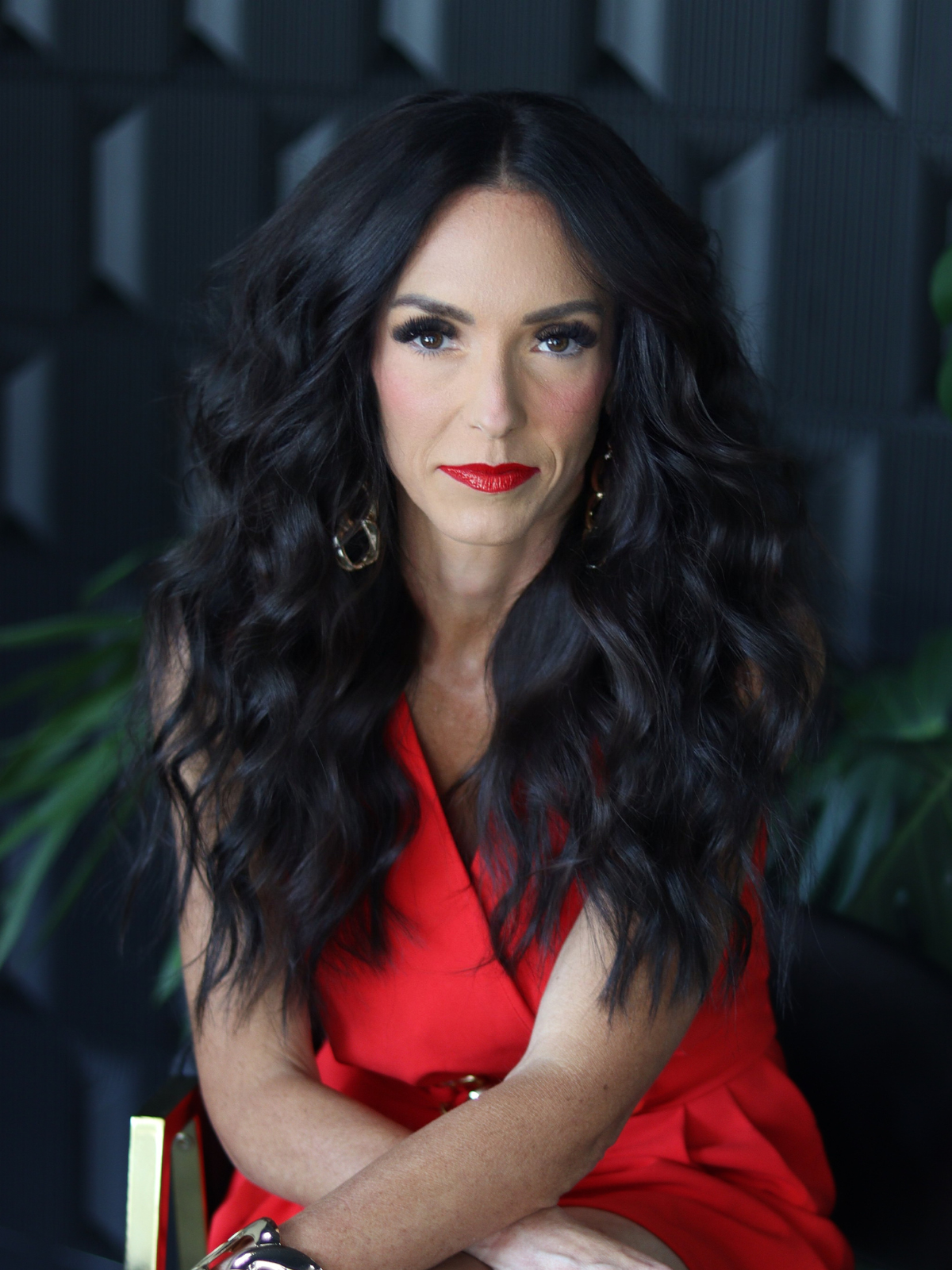 A woman in a red dress is sitting on a chair with her arms crossed.