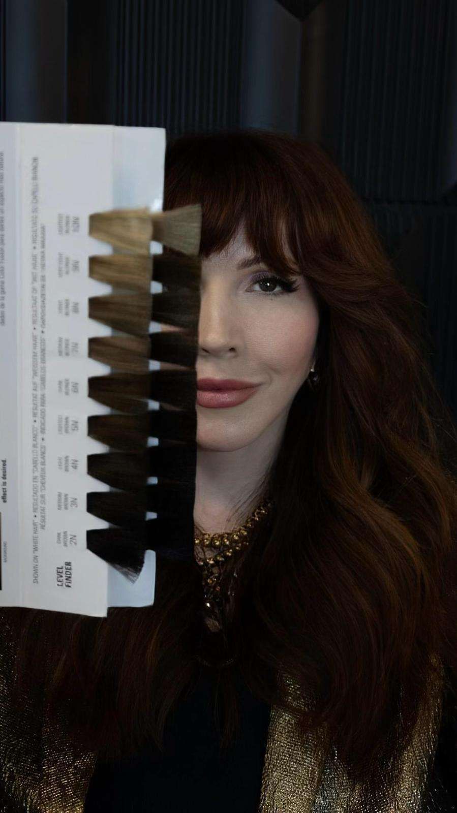 A woman is holding a palette of hair colors in front of her face.