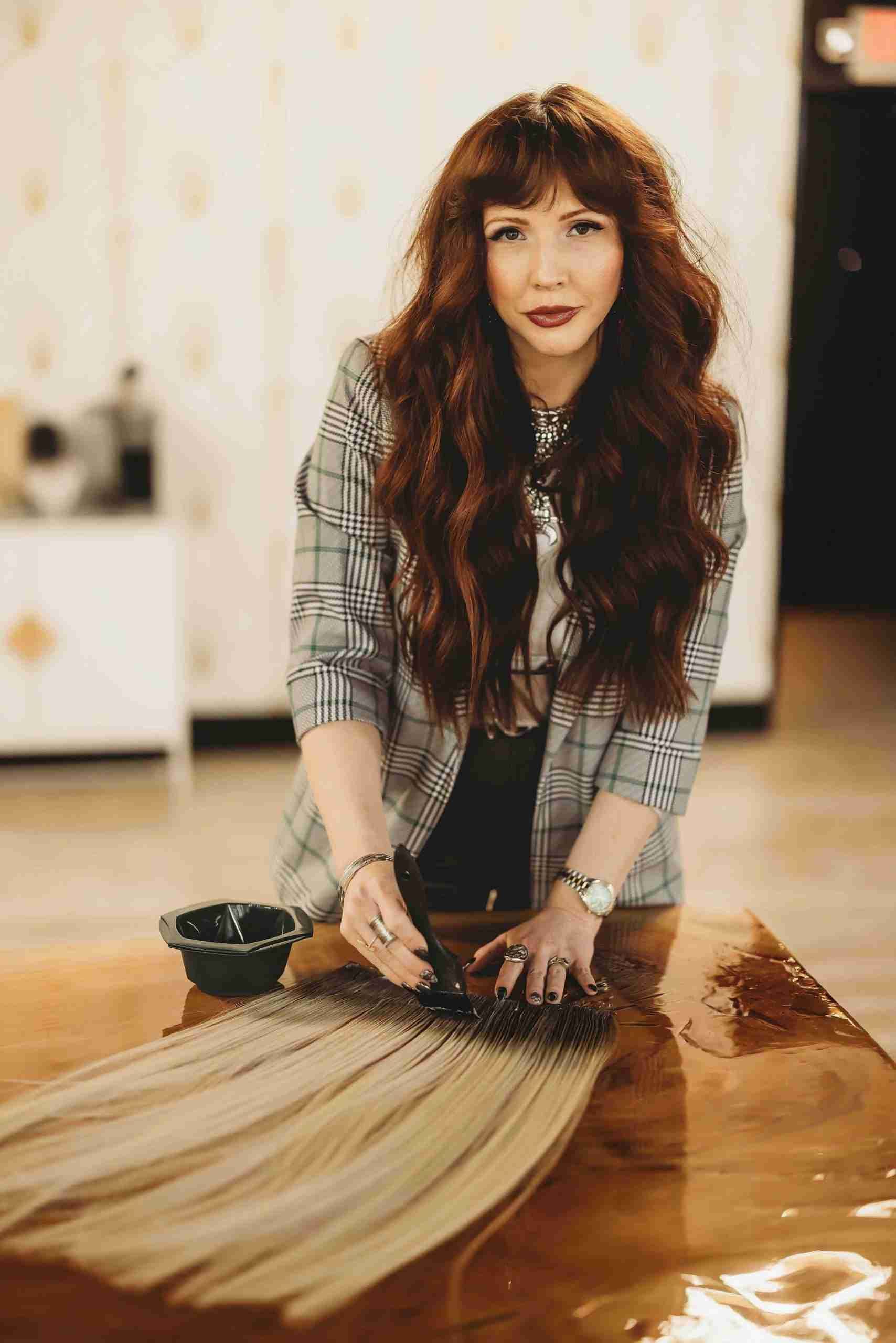 A woman with long red hair is sitting at a table with a bunch of hair extensions.