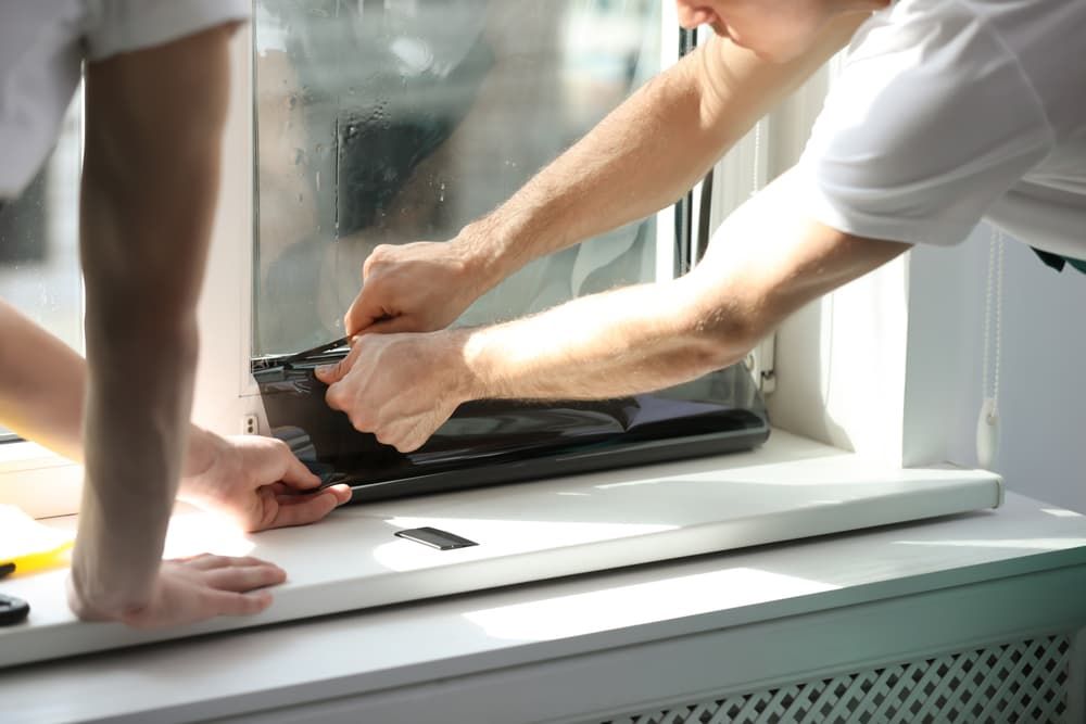 A Man Is Installing a Laptop on A Window Sill — Distinctive Glass & Aluminium in Kiama, NSW