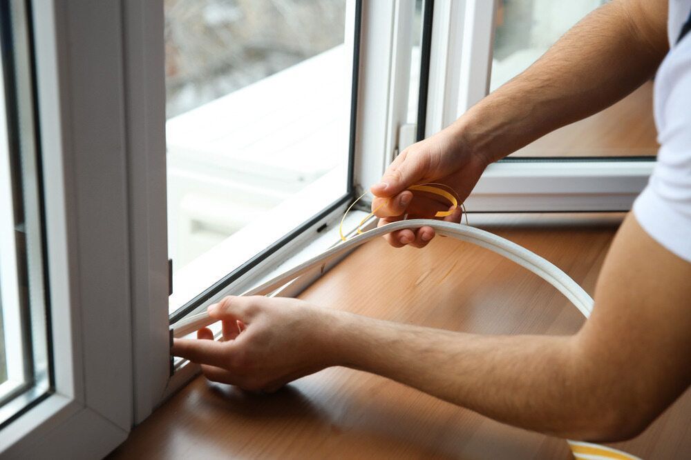 A Man Is Installing a Window Seal on A Window Sill — Distinctive Glass & Aluminium in Dapto, NSW