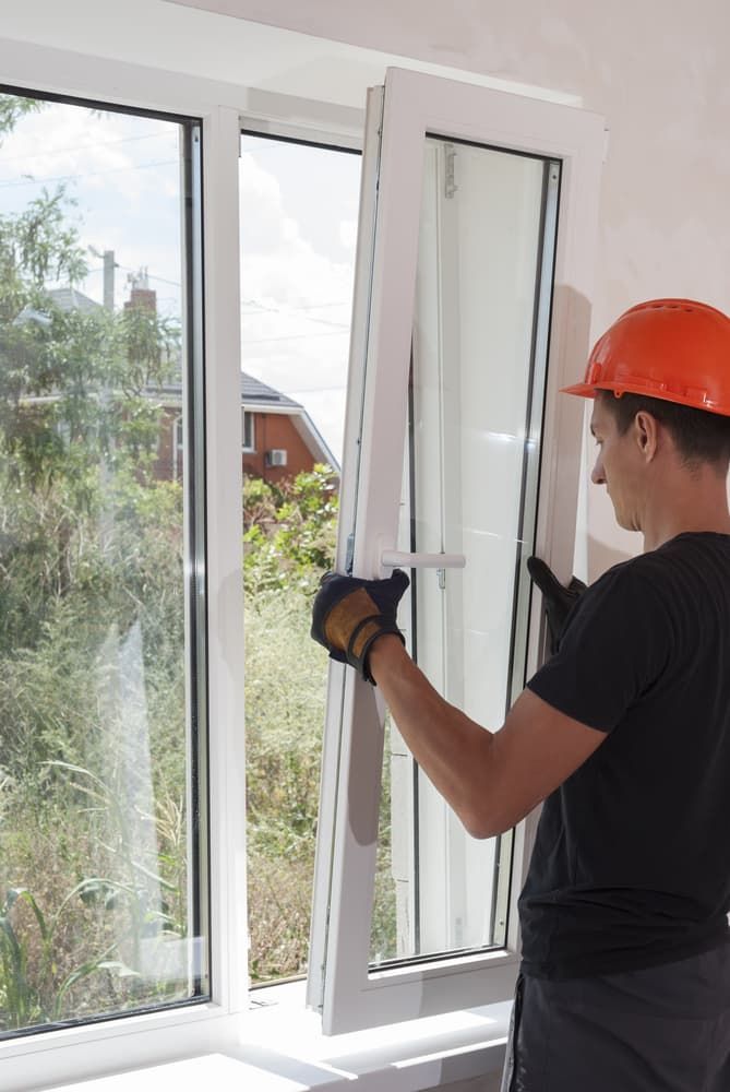 A Man Wearing a Hard Hat Is Installing a Window — Distinctive Glass & Aluminium in Kiama, NSW