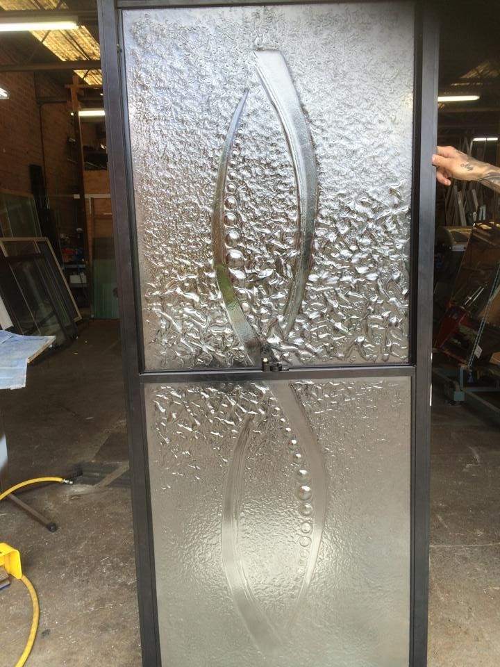 A Person Is Holding a Stained Glass Door in A Garage — Distinctive Glass & Aluminium in Kiama, NSW