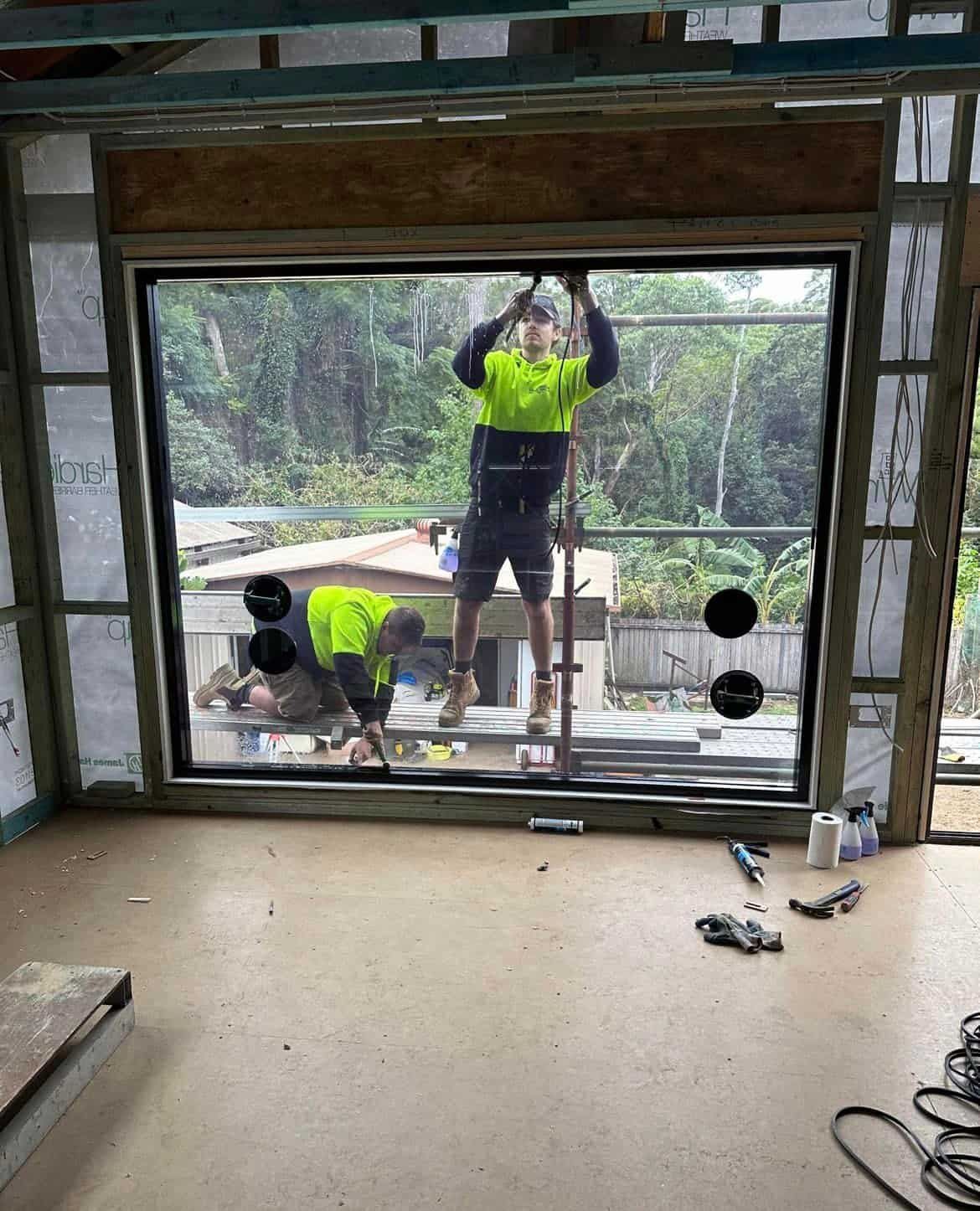 A Group of Men Are Working on A Window in A Room — Distinctive Glass & Aluminium in Dapto, NSW