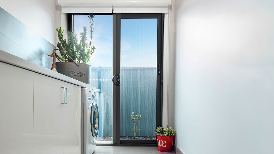 A Mesh Security Door with a black frame in a laundry room — Distinctive Glass & Aluminium in Port Kembla, NSW