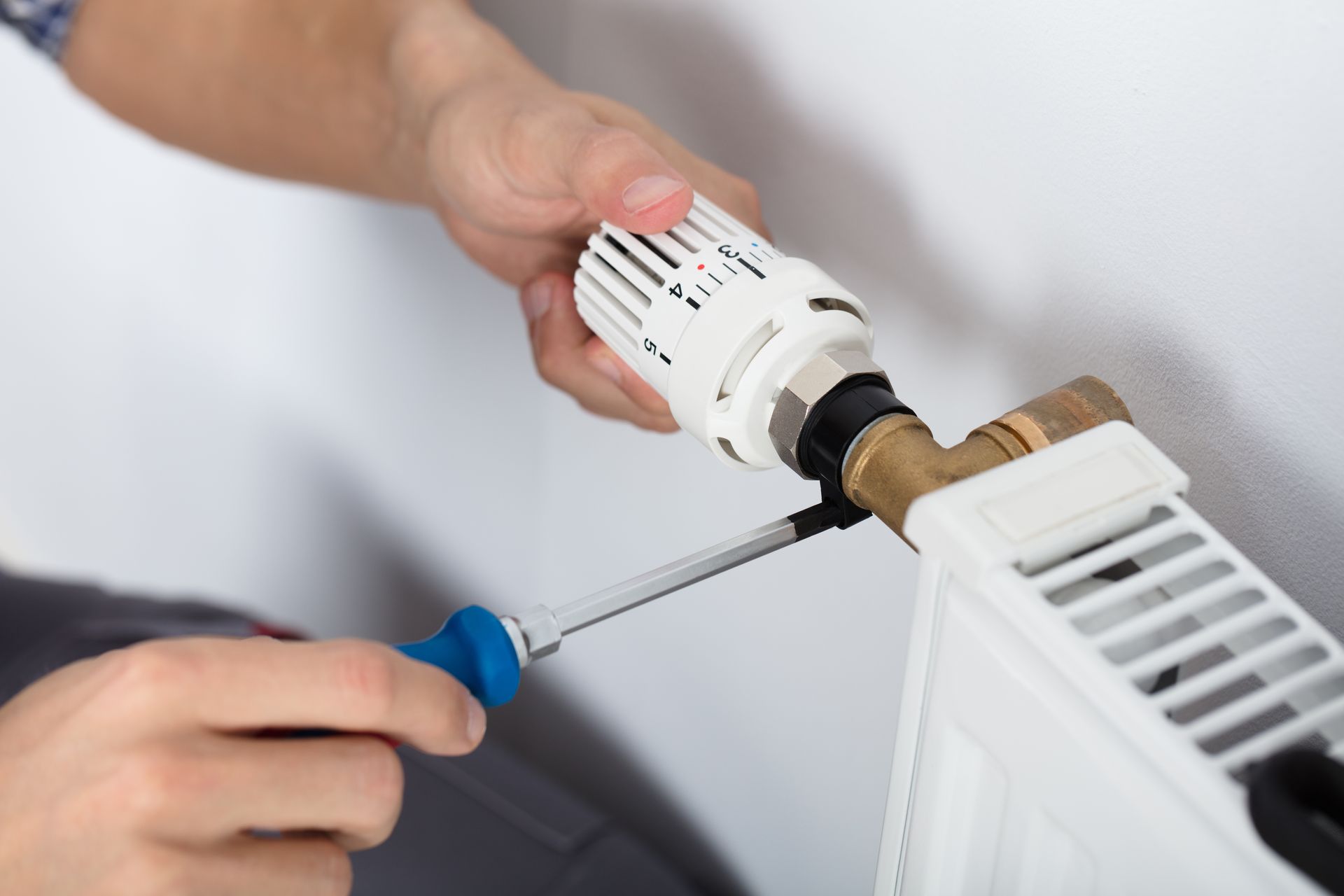 Person adjusts radiator valve with a screwdriver.