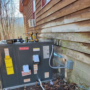 Goodman HVAC unit next to a wooden building, with tools on top, outdoors.