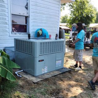 HVAC unit outside a building, with two people in blue shirts standing nearby, likely installing it.