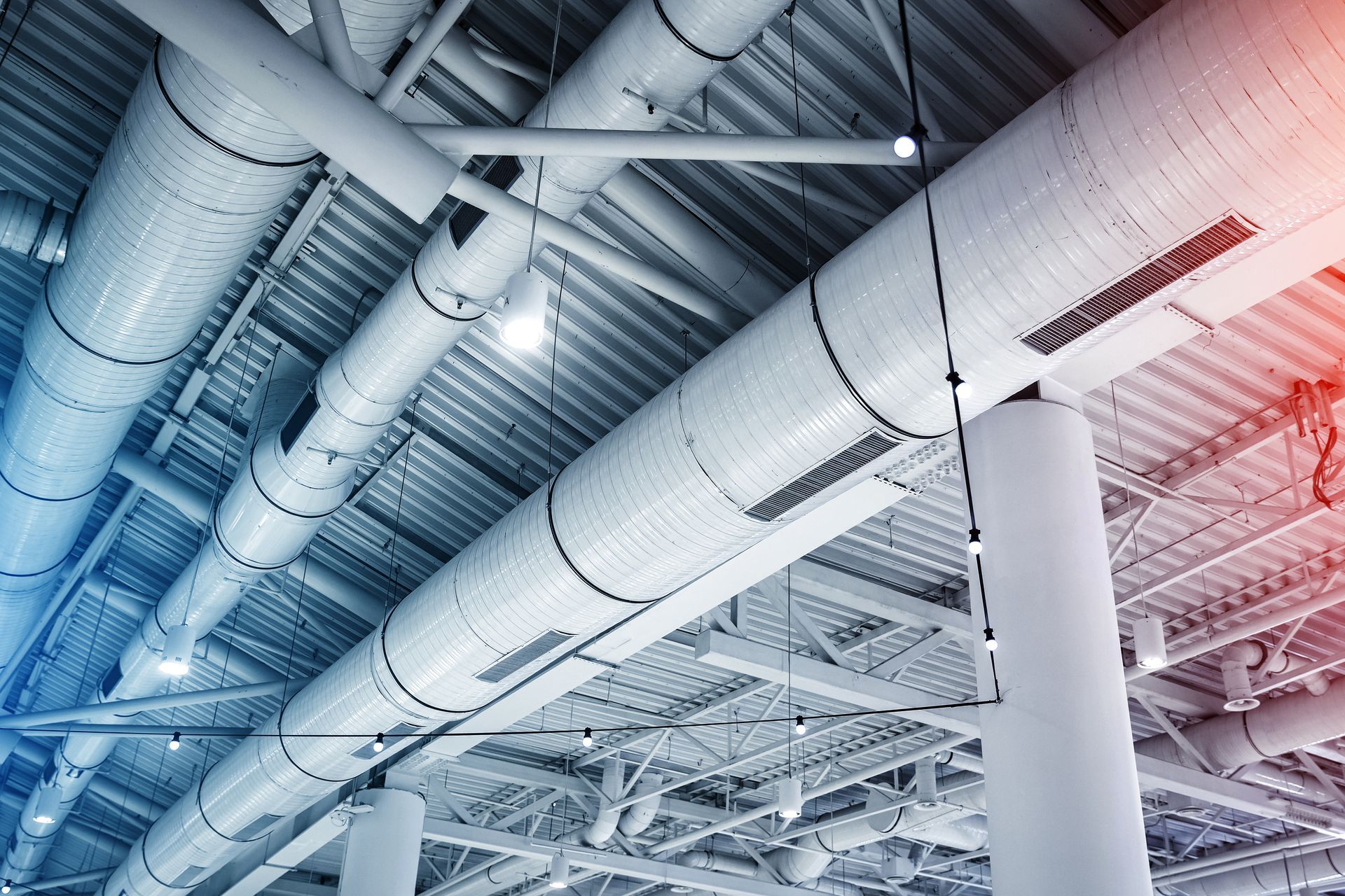 White industrial ceiling with large ventilation ducts, exposed beams, and lights.