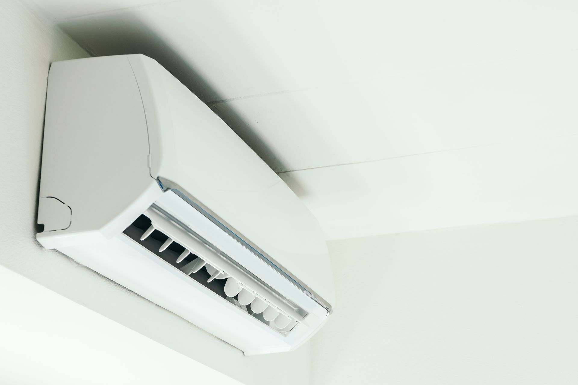 A technician wearing a face mask services a wall-mounted air conditioning unit.
