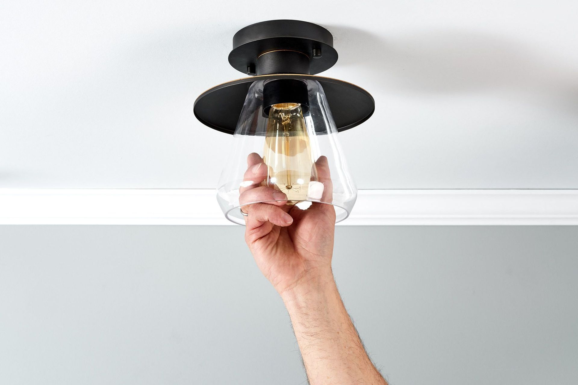 Hand reaching to install a lightbulb in a black and glass ceiling fixture against a white ceiling.