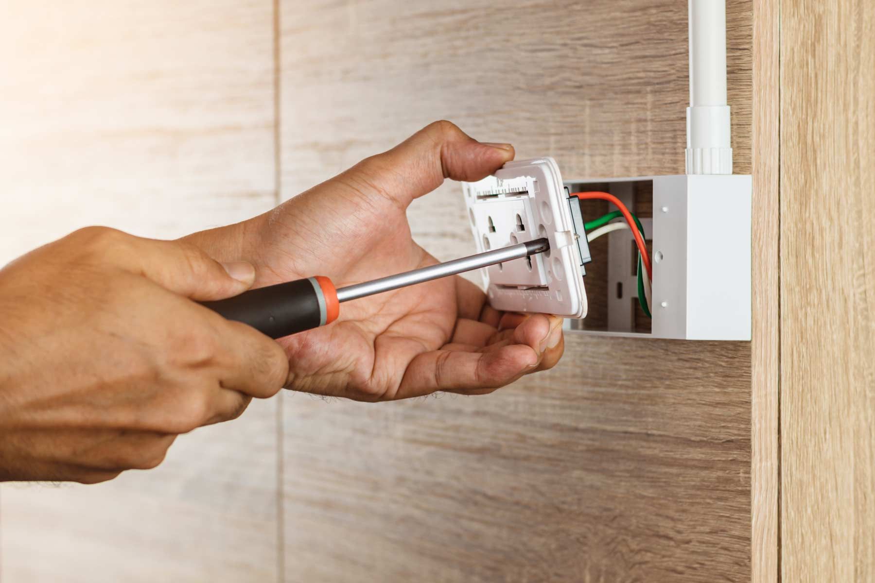 Person using a screwdriver to install a white electrical outlet in a wall.