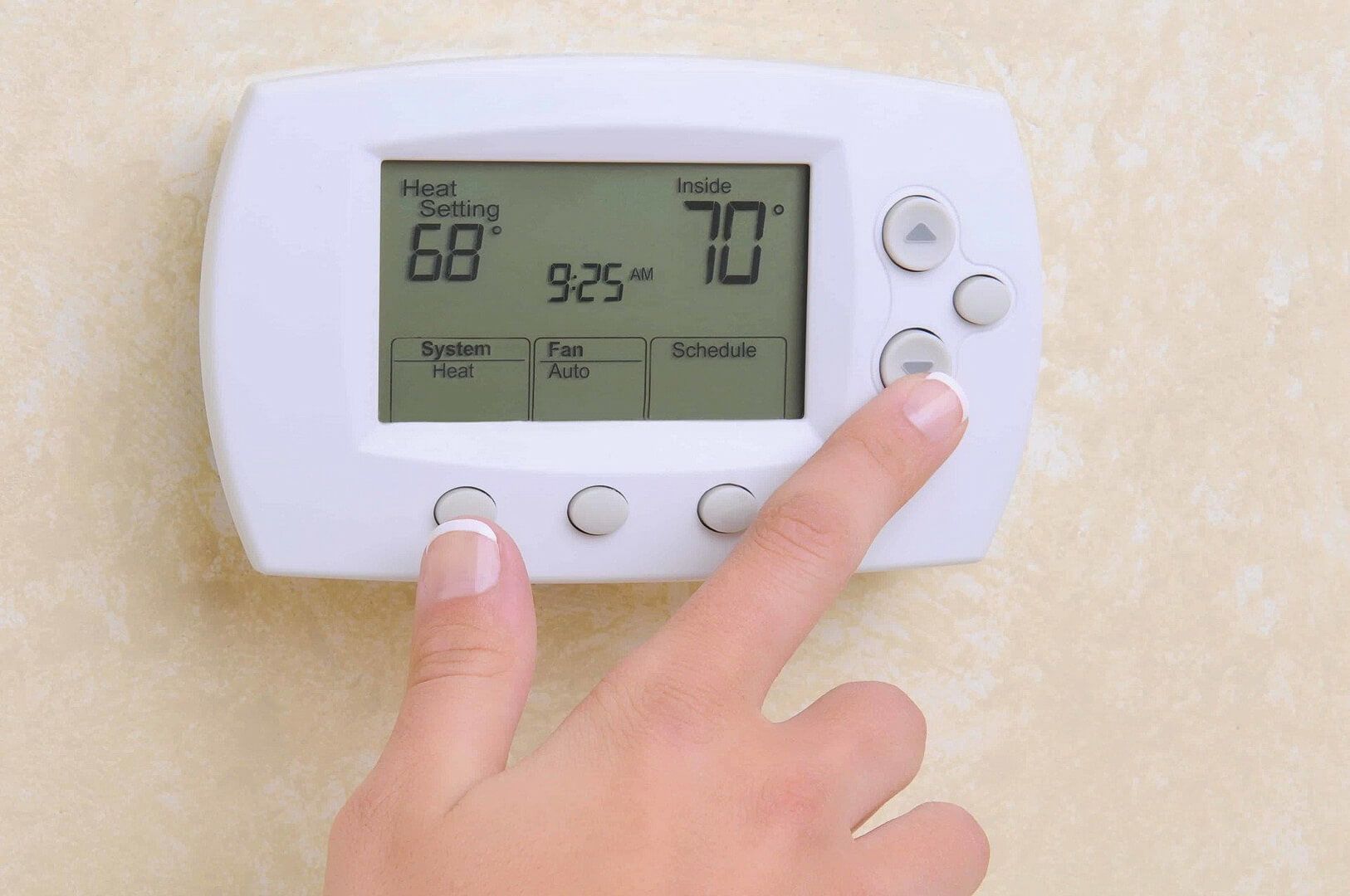 Hand adjusting a white digital thermostat showing 70°F and 92.5° on its display.