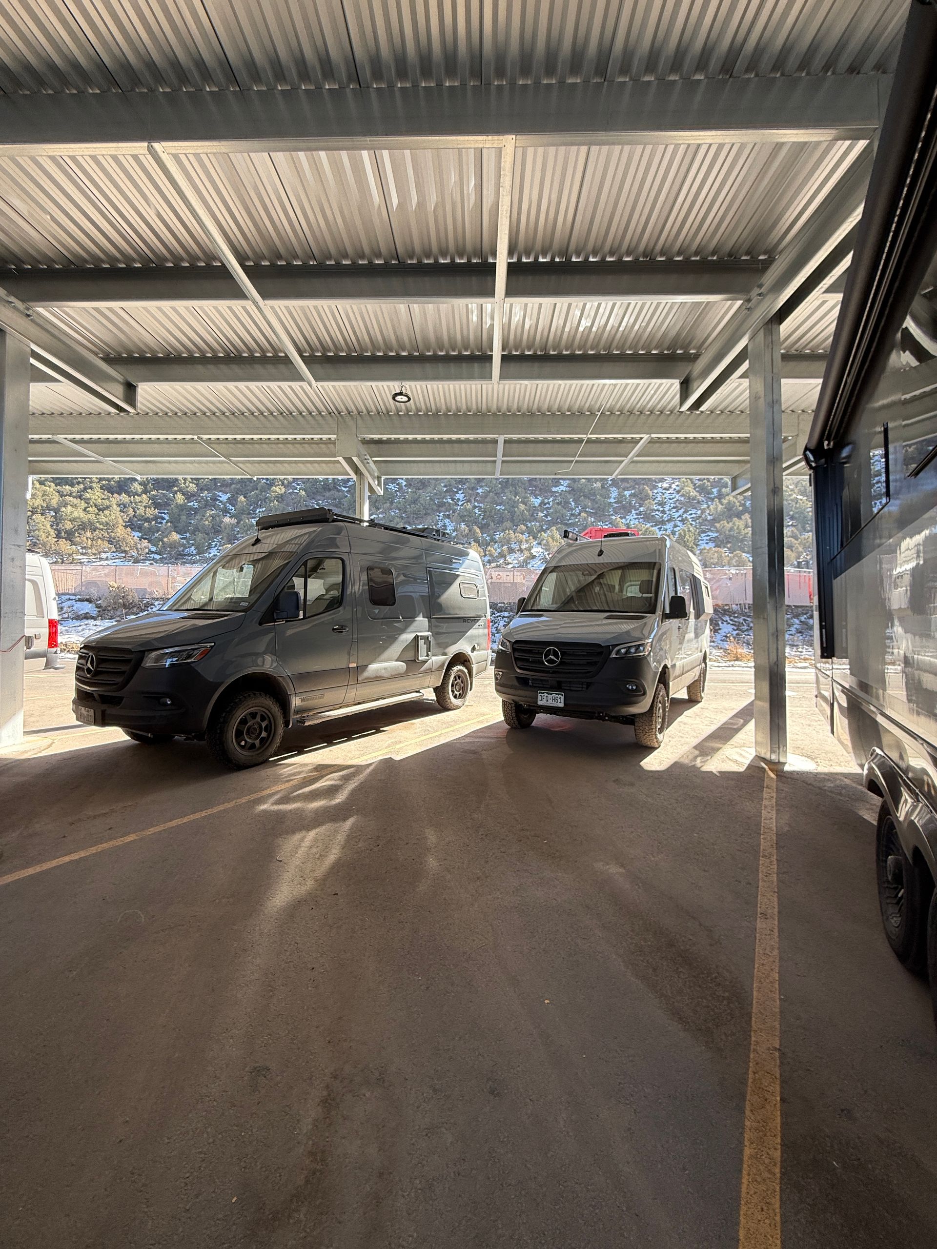 Class B camper vans parked under steel canopy with electric hookups
