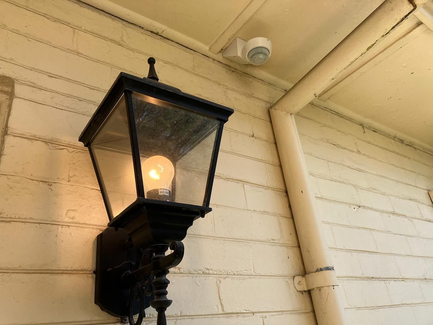 Black lantern and white motion sensor on a cream-colored wall.