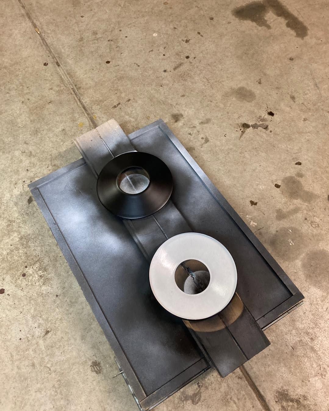 Metal plate with two large washers, one black, one white, on a concrete surface.