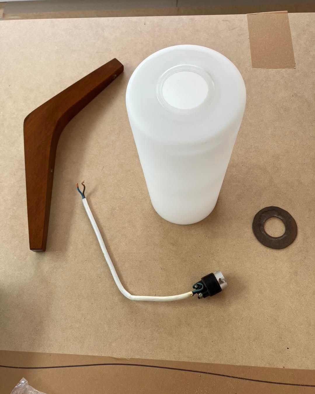 Wooden lamp leg, white cylindrical shade, electrical cord, and a small metal washer on a brown surface.